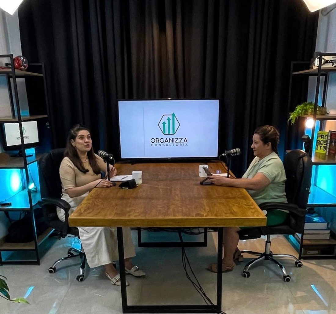 Estúdio do Podcast Organizza, com duas pessoas conversando à mesa e o logo da Organizza na tela